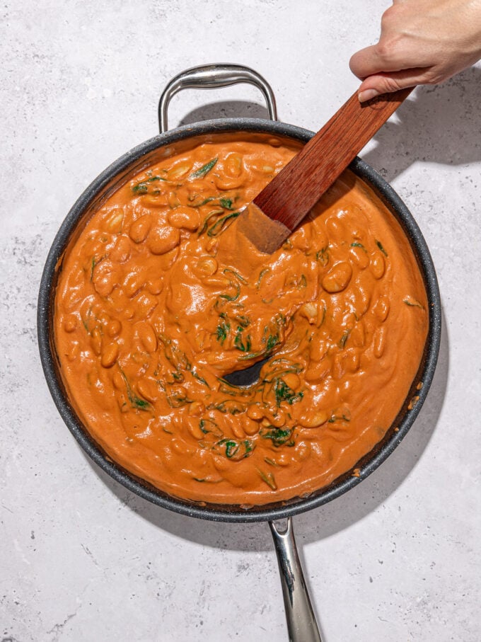 hand stirring creamy rose butter beans in skillet