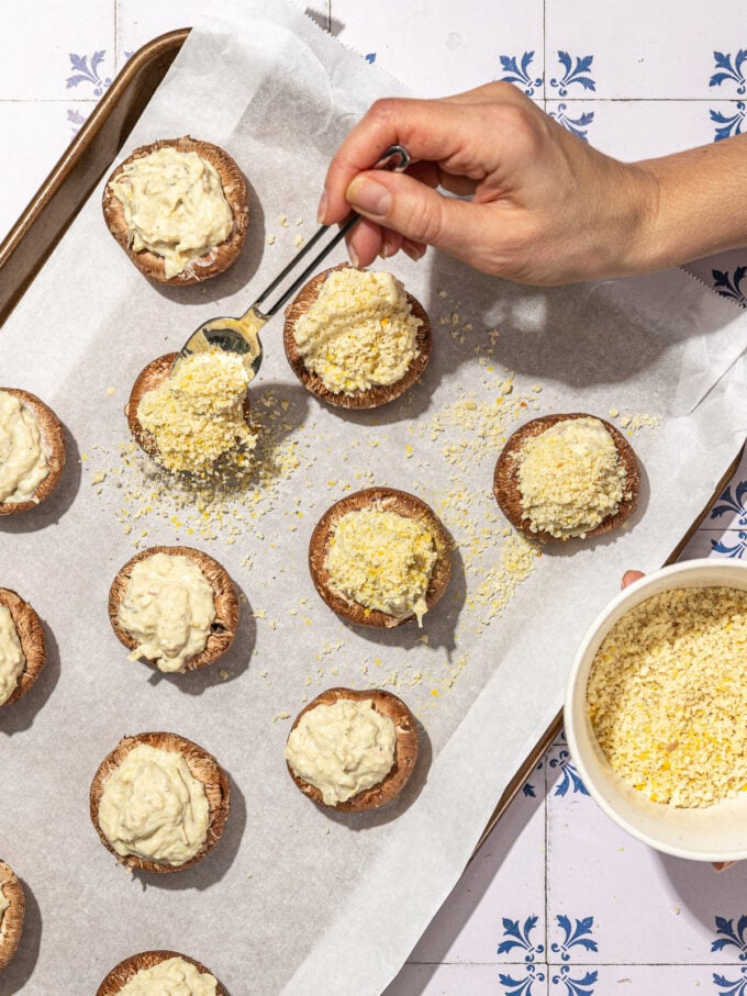 hand spooning panko crumbs over vegan stuffed mushrooms on baking sheet