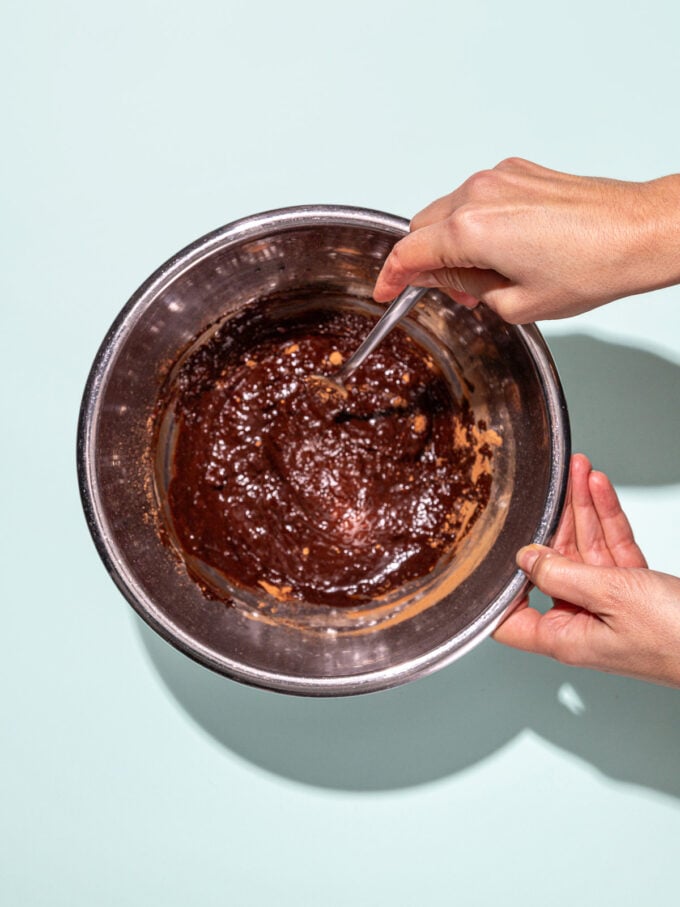 hand stirring chocolate mixture in metal bowl