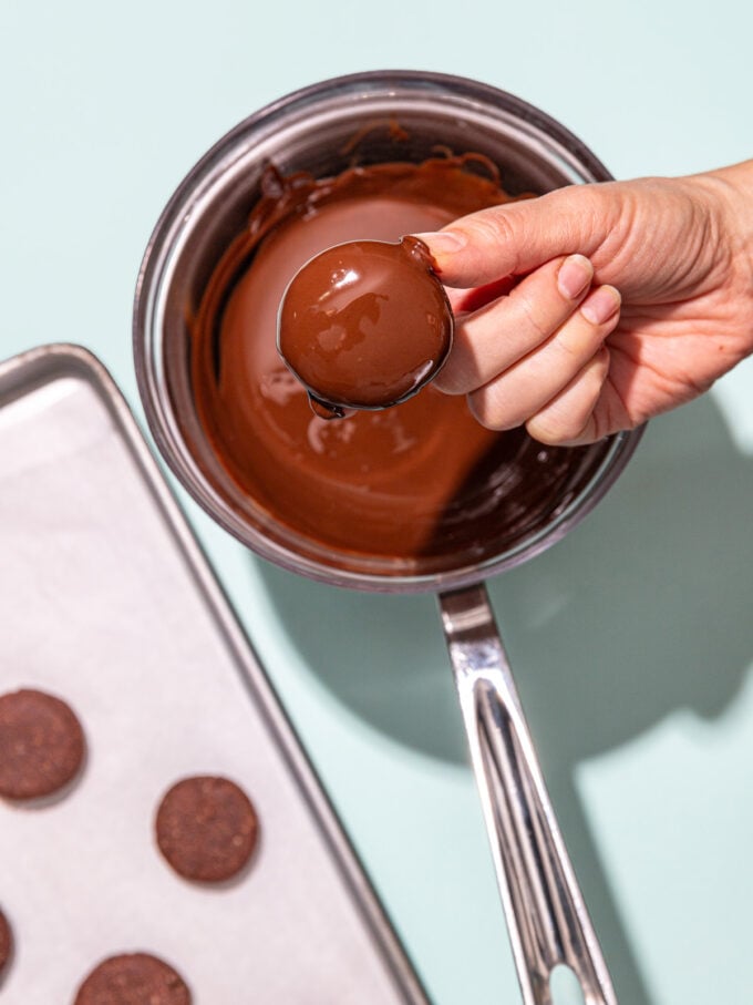 hand holding chocolate dipped cookie over pot of melted chocolate 