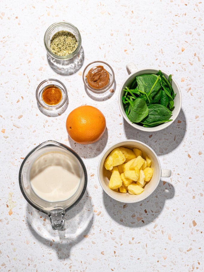 bowls of soy milk, spinach, pineapple and an orange