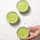 three glasses of green smoothies and hand holding glass