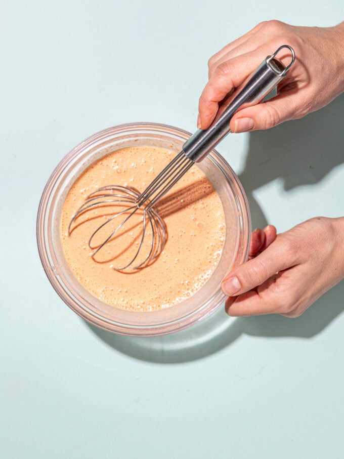 hand whisking red curry sauce in glass bowl