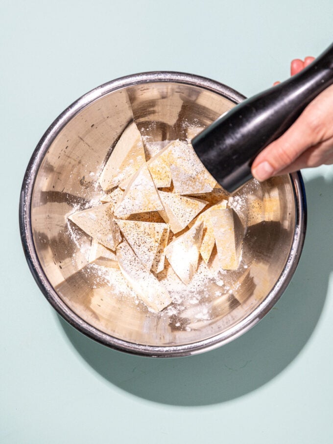 hand cracking pepper into metal bowl of tofu
