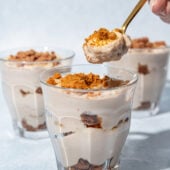 hand holding a spoonful of banana biscoff pudding with dessert glasses