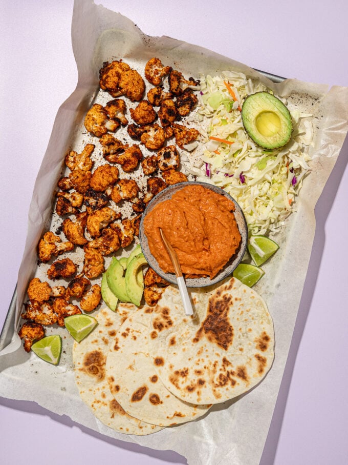 roasted cauliflower, tortillas, cheese, avocado and chipotle sauce on baking sheet