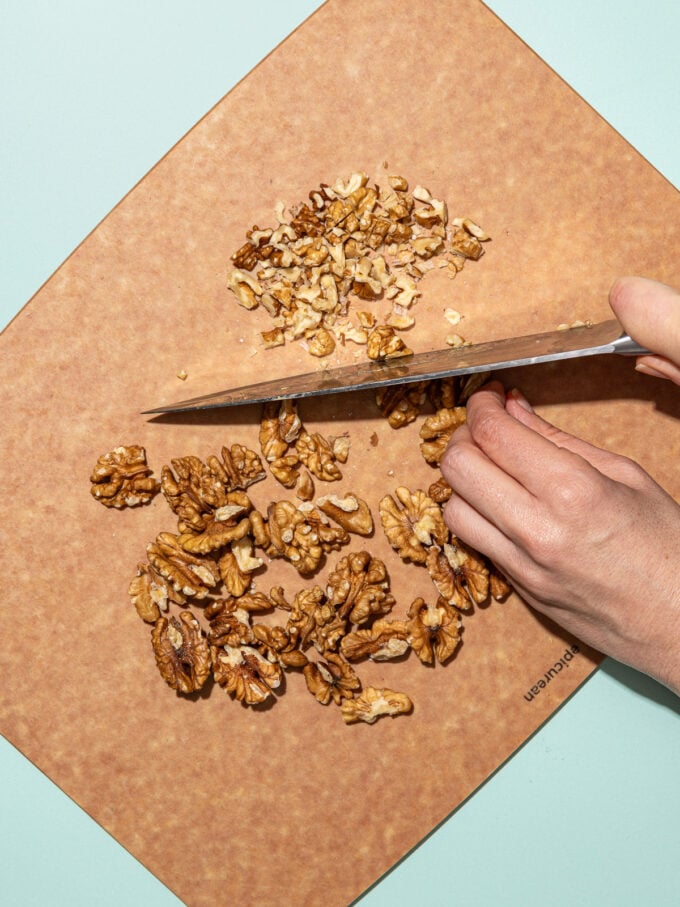 hand chopping walnuts on a wood cutting board
