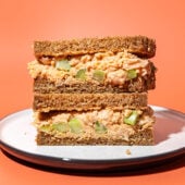stacked chickpea salad sandwich on white plate with orange background