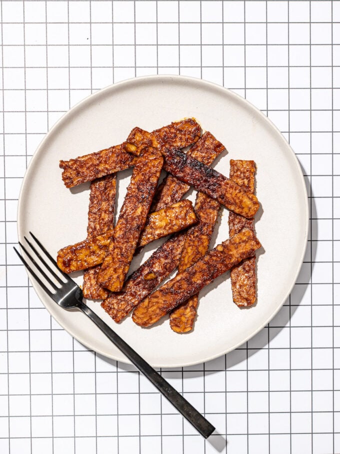 slices of tempeh bacon on white plate with black fork