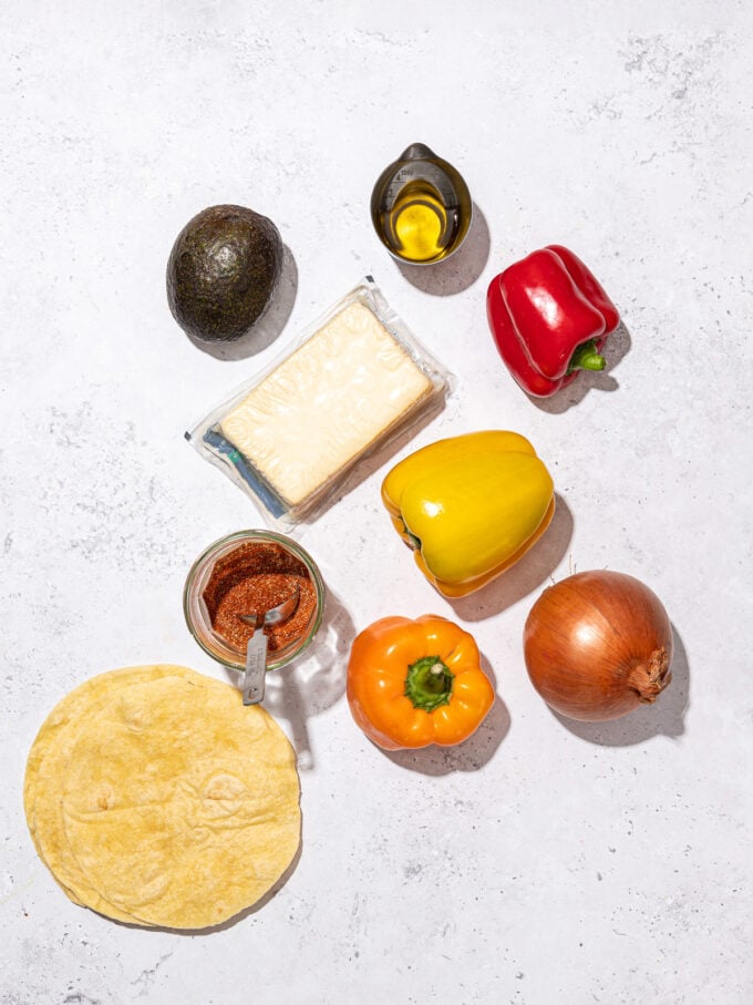 bell peppers, onion, tofu, tortillas, avocado and bowl of fajita seasoning on grey background